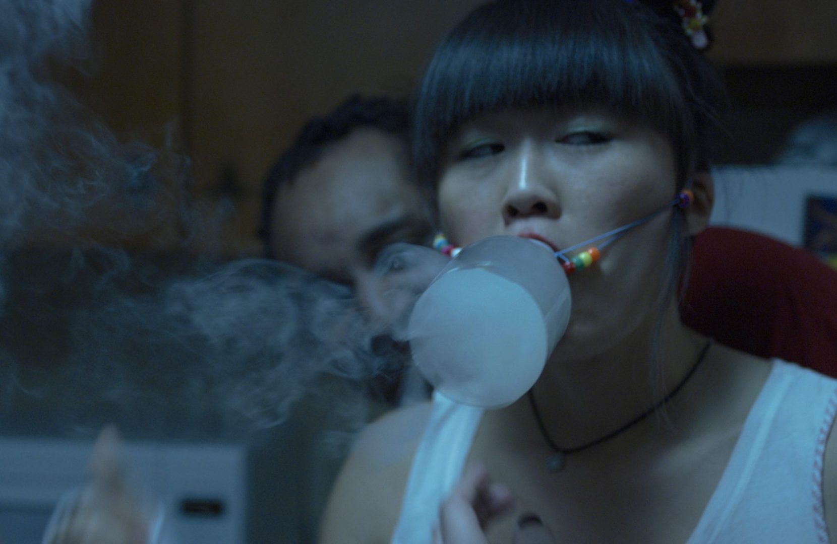 Still from Wallflower film. Woman inhales drug-infused smoke from a bottle strapped to her face.